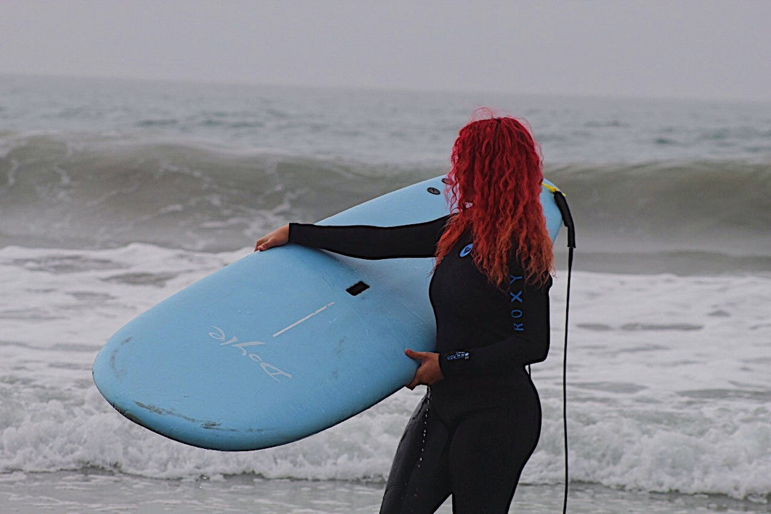 A woman in a wetsuit at the beach holding a surf board.