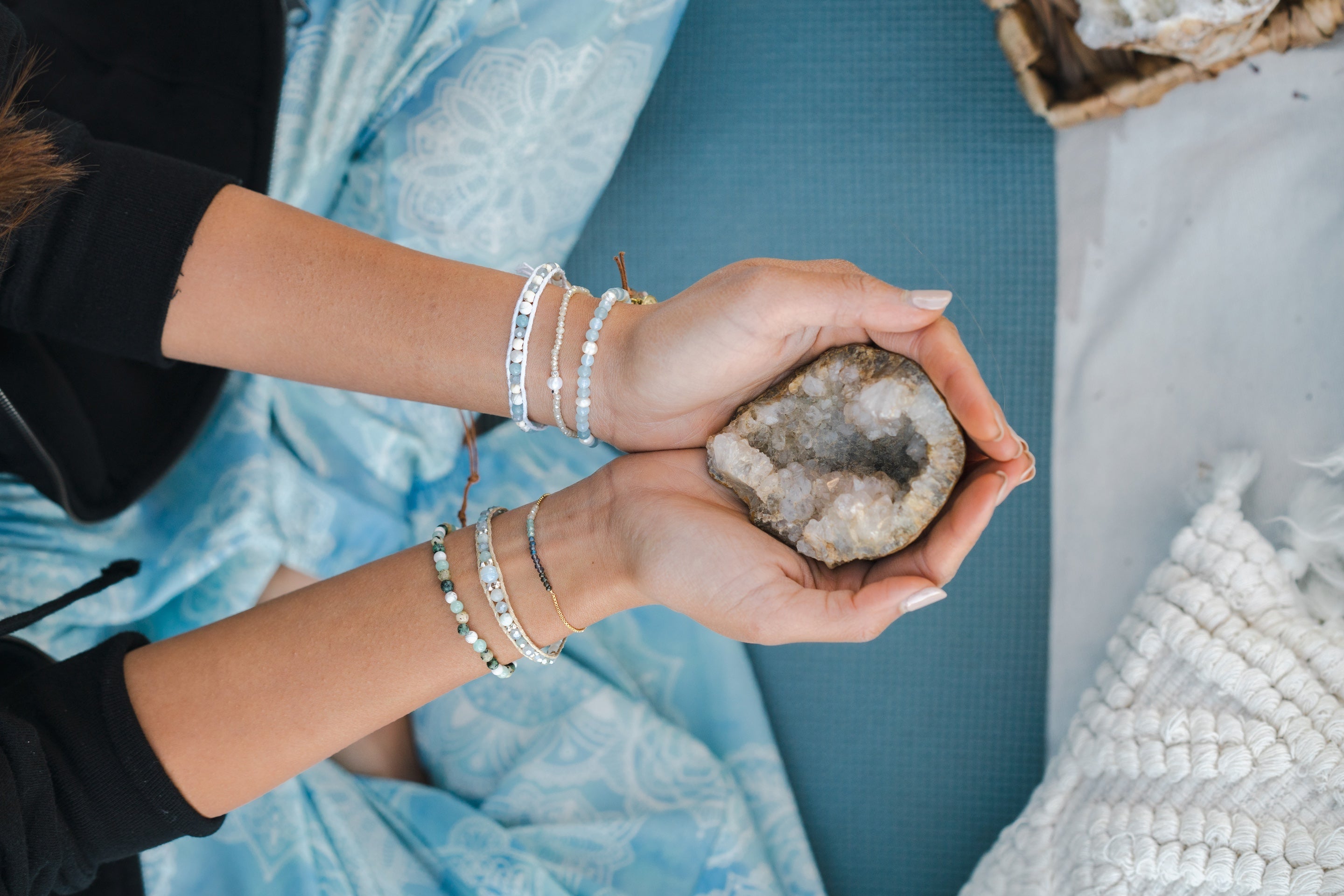 Woman's wrist and hands wearing natural stone bracelets and holding a large crystal.