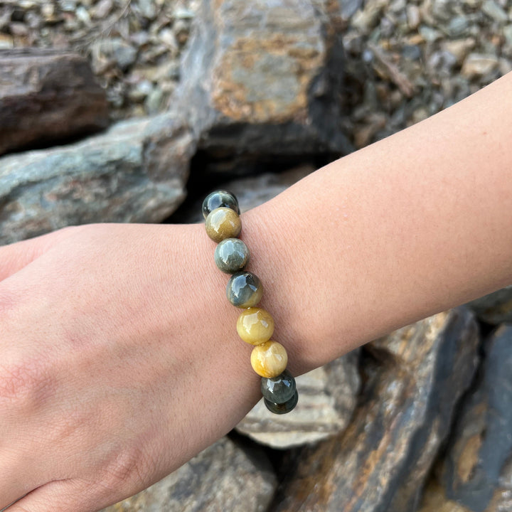 A close-up of a woman's wrist wearing a dream tigers eye stretch style bracelet made with 10mm beads on a stretch cord, with gray and tan rocks in the background.