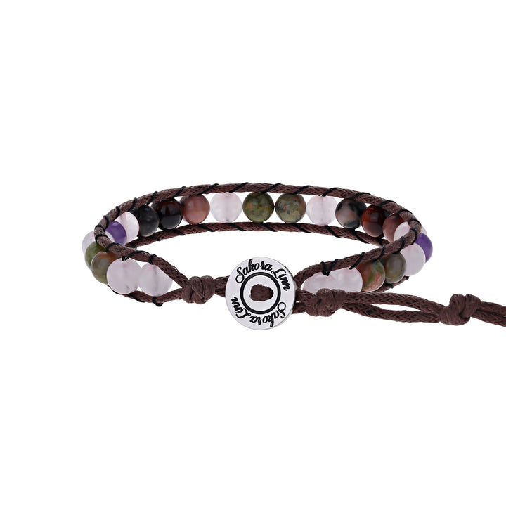 Close-up of a wrap style bead bracelet made with 6mm rose quartz, amethyst, and rhodonite, in shades of pink, green, black, purple and brown colors, strung on an adjustable brown cord, with a silver logo button closure stamped in black wth Sakora Linn, displayed on a white background.