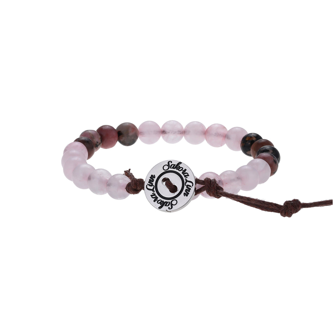 Close-up of a bead bracelet made with 6mm rose quartz and rhodonite beads, in shades of pink, black, and green colors, strung on an adjustable brown cord, with a silver color logo button closure stamped in black wth Sakora Linn, displayed on a white background.