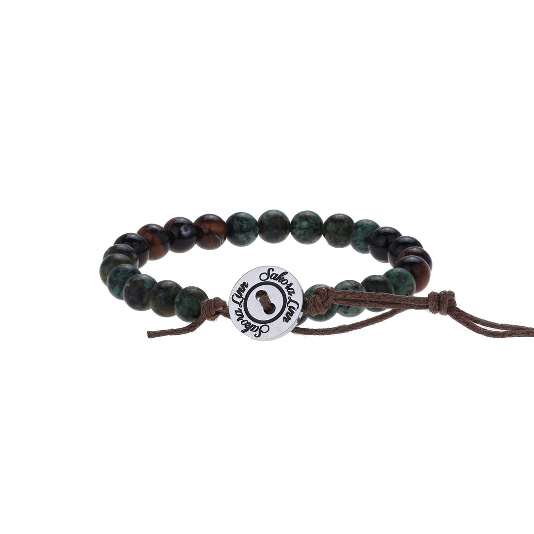Close-up of a bead bracelet made with 6mm tiger's eye and african turquoise beads, in sahdes of brown, green, and black, strung on an adjustable brown cord, with a silver color logo button closure stamped in black wth Sakora Linn, displayed on a white background.