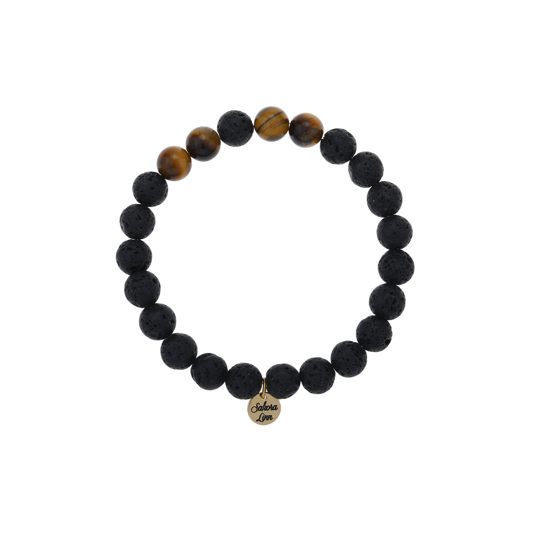 Close-up of a stretch style lava stone and tiger's eye bracelet made with 8mm round black lava stone beads with four 8mm tiger's eye beads on each side of one black center bead, in black and brown colors, with an 18k gold plated logo tag engraved with Sakora Linn, displayed on a white background.