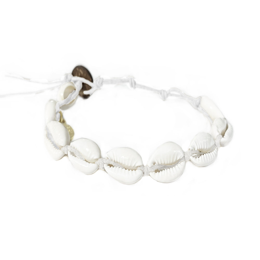 Close-up of a cowry shell bracelet made with nine white cowry sea shells strung on an adjustable white cord with a dark brown coconut shell button closure displayed on a white background.
