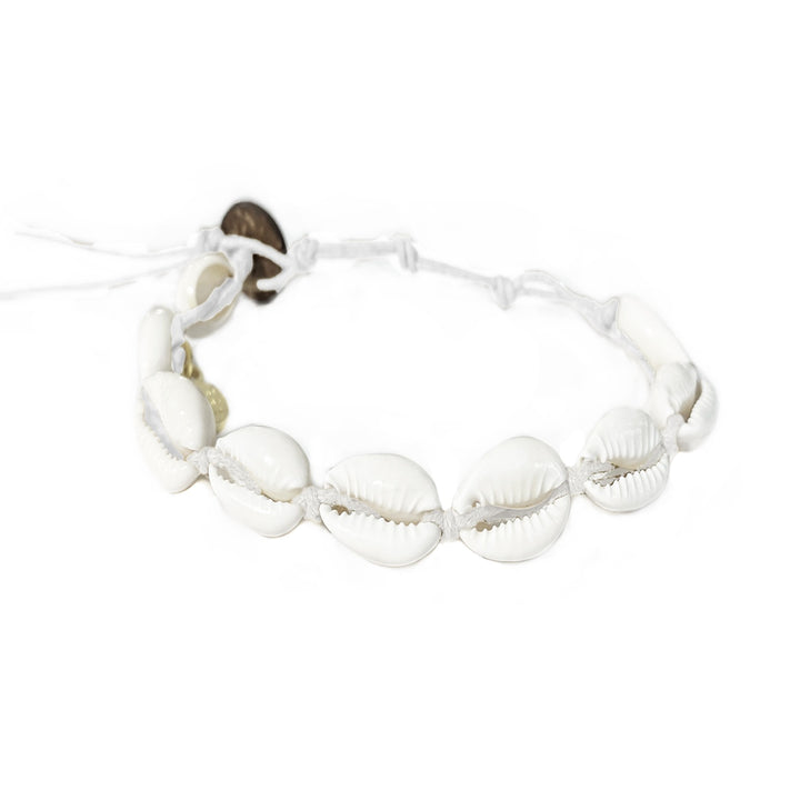 Close-up of a cowry shell bracelet made with nine white cowry sea shells strung on an adjustable white cord with a dark brown coconut shell button closure displayed on a white background.