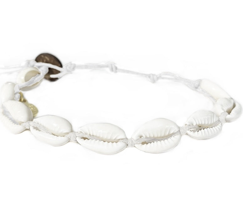 Close-up of a cowry shell bracelet made with nine white cowry sea shells strung on an adjustable white cord with a dark brown coconut shell button closure displayed on a white background.