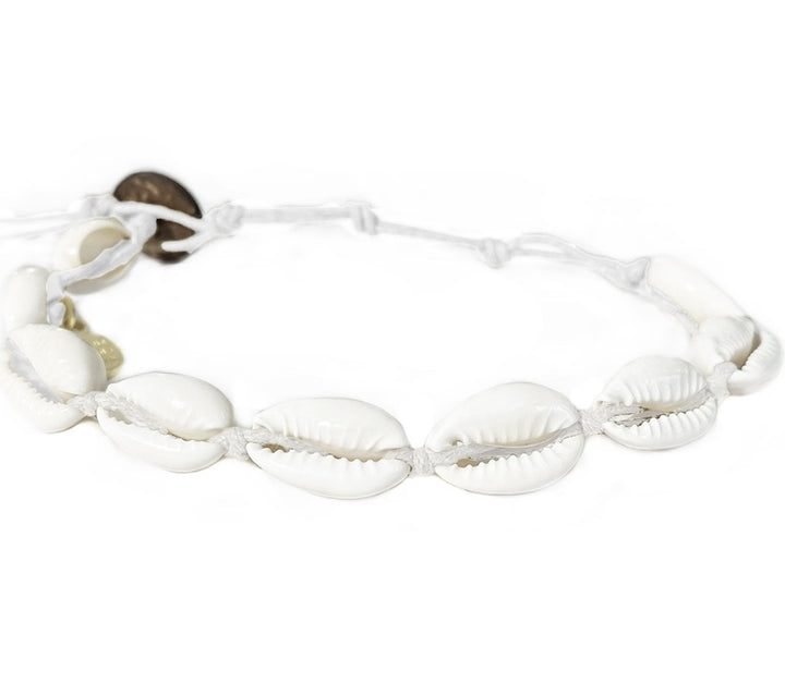 Close-up of a cowry shell bracelet made with nine white cowry sea shells strung on an adjustable white cord with a dark brown coconut shell button closure displayed on a white background.