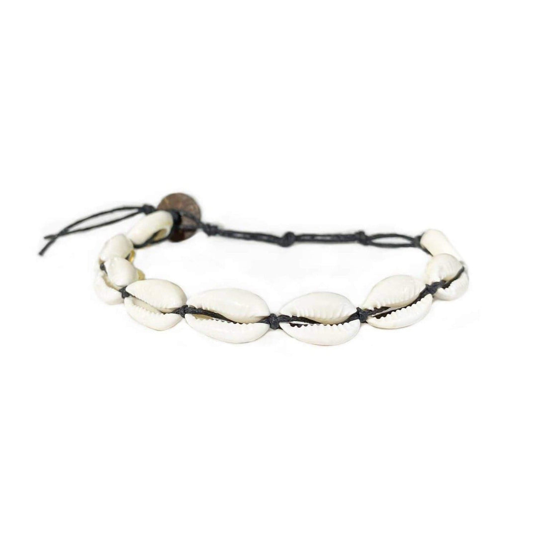 Close-up of a cowry shell bracelet made with nine white cowry sea shells strung on an adjustable black cord with a dark brown coconut shell button closure displayed on a white background.