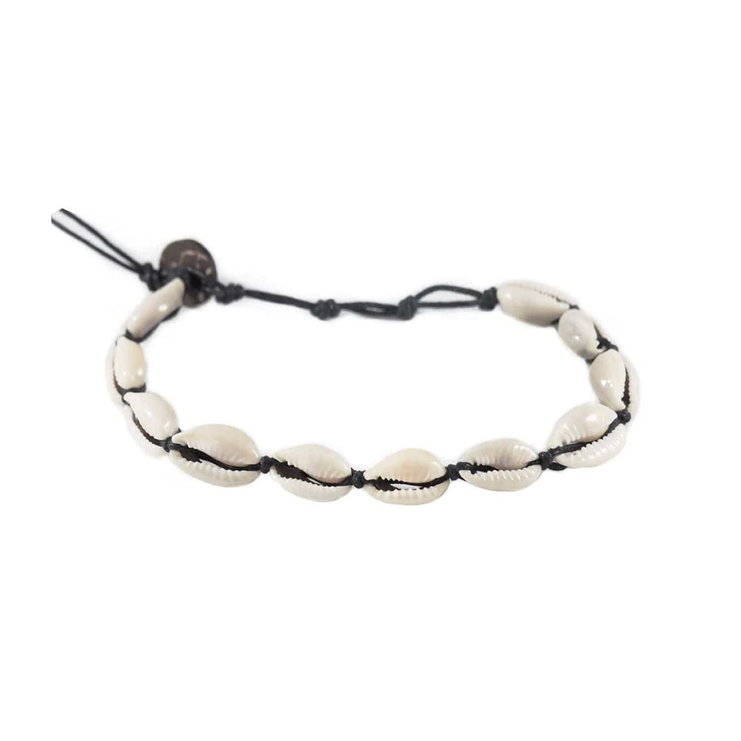 Close-up of a sea shell ankle bracelet made with white cowry sea shells, and an adustable black cord and a dark brown coconut shell button closure, displayed on a white background.