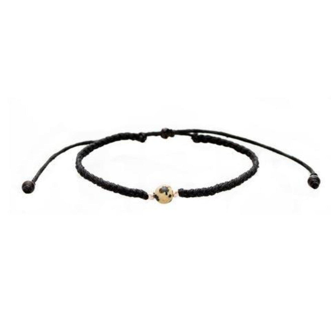 Close-up of a black braided slip knot syle bracelet with a dalmatian spotted cream and black jasper stone in the center and small silver accent beads on each side of the stone, displayed on a white background.