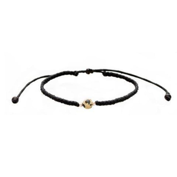 Close-up of a black braided slip knot syle bracelet with a dalmatian spotted cream and black jasper stone in the center and small silver accent beads on each side of the stone, displayed on a white background.