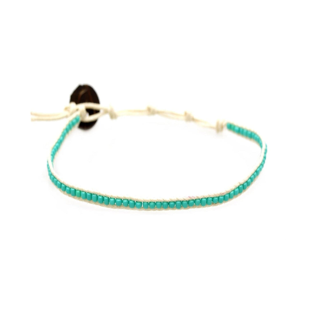 Close-up of a seed bead ankle bracelet made with turquoise seed beads, with an adustable cream colored cord and a dark brown coconut shell button closure.