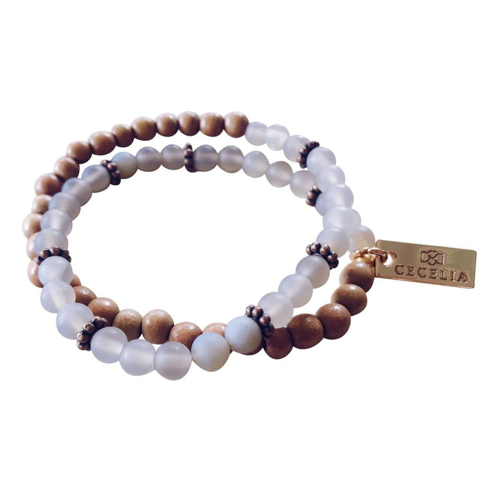 A stretch syle double-wrap bracelet made of frosted gray, and brown wood, beads with copper accent beads, and a gold-tone logo tag, displayed on a white background.