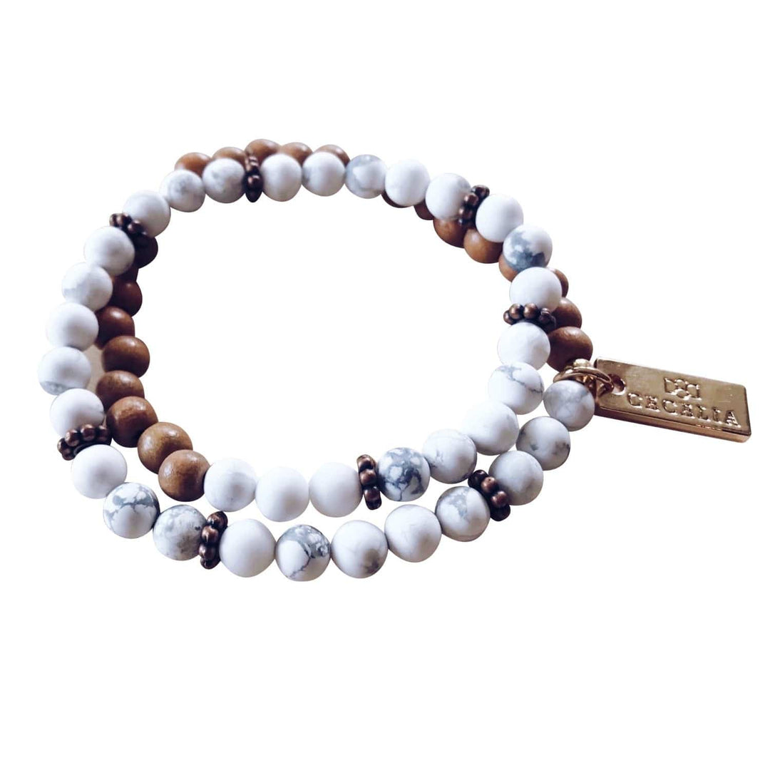 A stretch syle double-wrap bracelet made of white gray howlite, and brown wood, beads with copper accent beads, and a gold-tone logo tag, displayed on a white background.