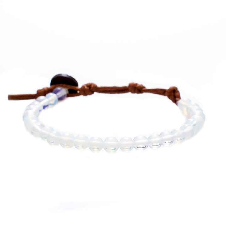Close-up of a bead bracelet made with 6mm iridescent blue moonstone beads, and a brown adjustable cord and dark brown coconut shell button closure, displayed on a white background.