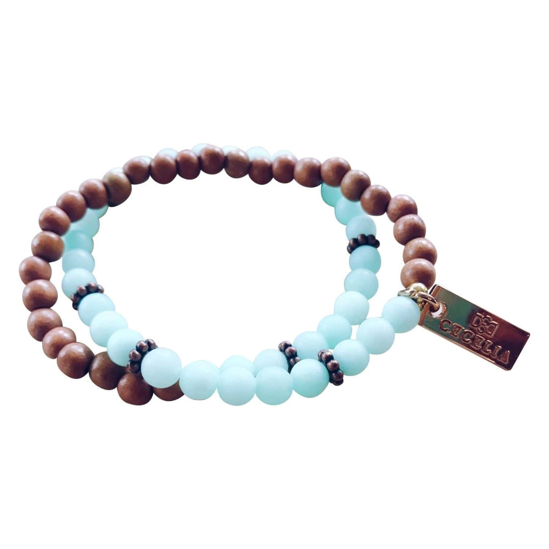 A stretch syle double-wrap bracelet made with light blue jade, and brown wood, beads with copper accent beads, and a gold-tone logo tag, displayed on a white background.