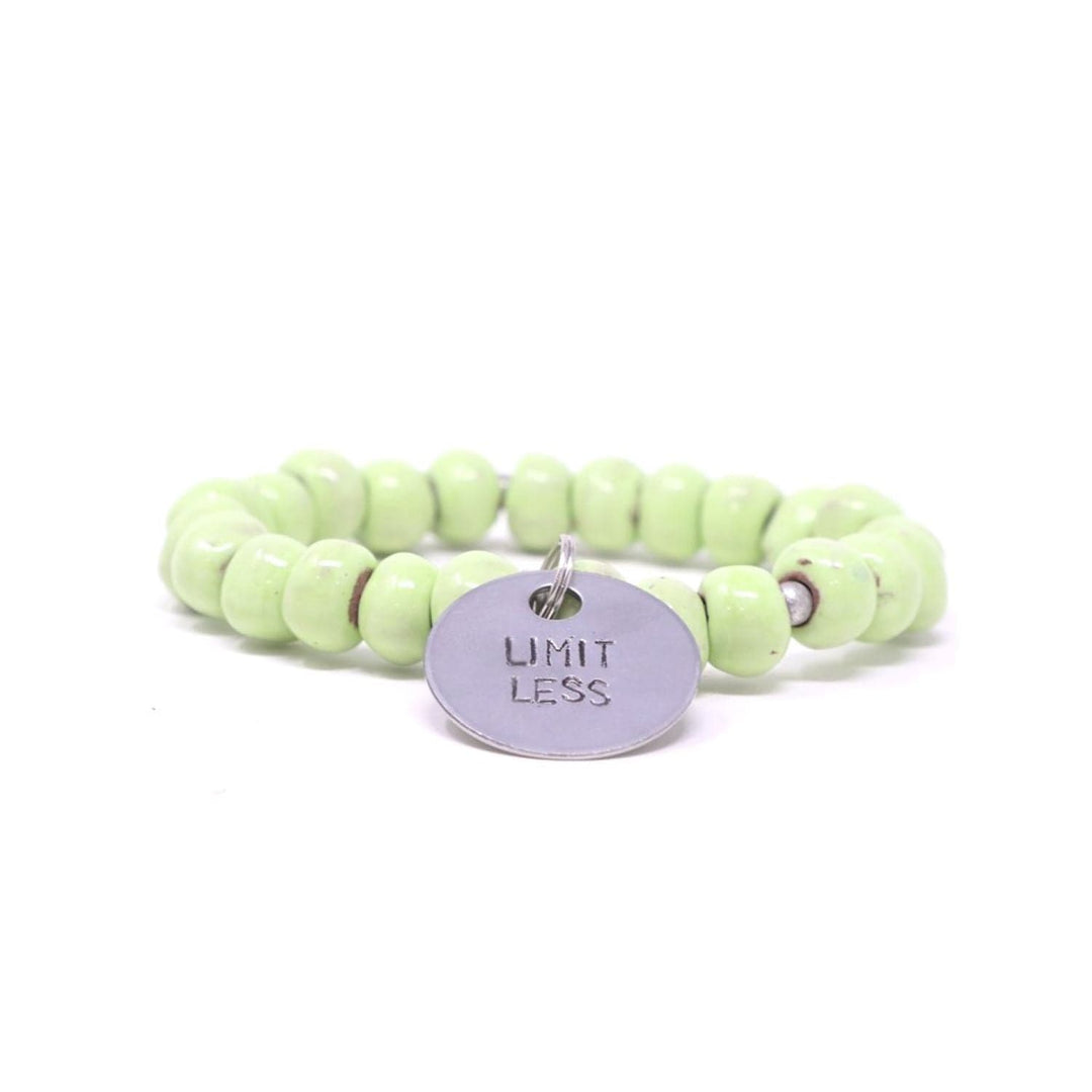 Close-up of a stretch style bracelet made with pale green clay beads and silver accent beads, with a silver metal charm with the inscription 'LIMITLESS', displayed on a white background.