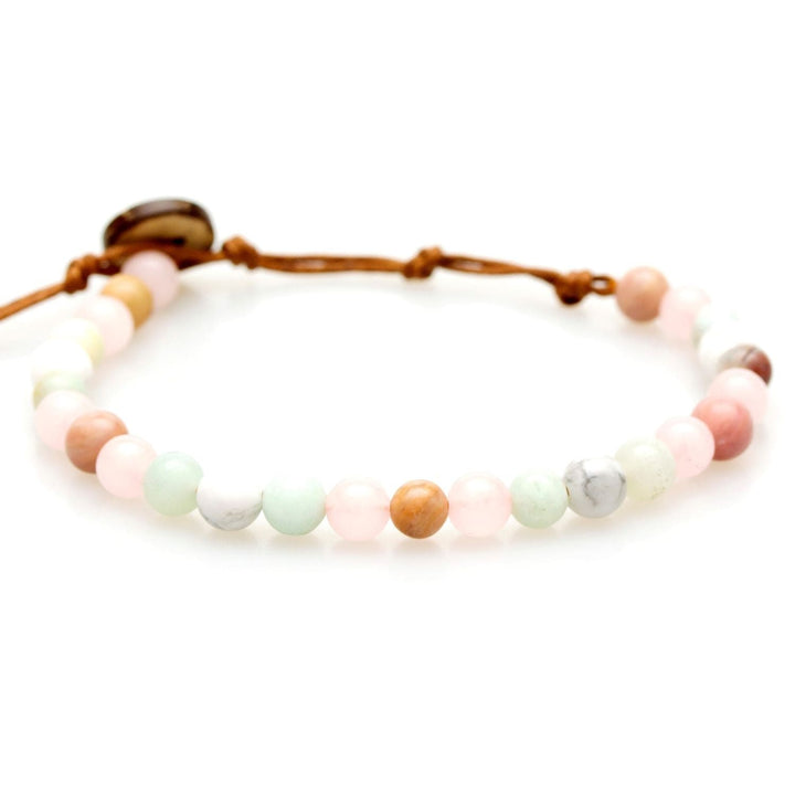 Close-up of a healing style bracelet made of rose quartz and howlite 6mm beads, in light pink, light green, white, and tan colors, strung on an adjustable brwon cord with a darker brown coconut shell button closure, displayed on a white background.