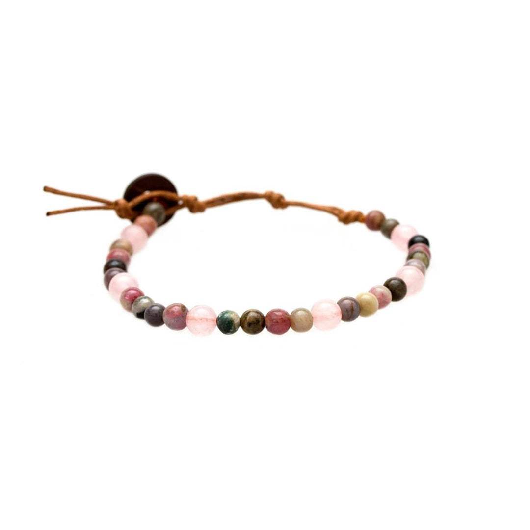 Close-up of a healing bead bracelet with round 6mm rose quartz and tourmaline beads in shades of purple, pink, green, and tan colors, with a adjustable brown cord and dark brown coconut shell button closure, displayed on a white background.