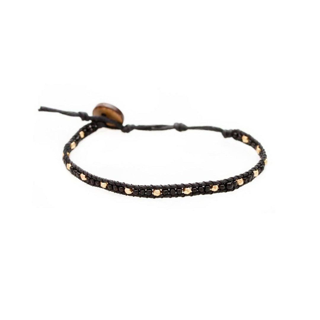 Close-up of a wrap style bead bracelet made with black and gold seed beads, and an adjustable black cord with a brown coconut shell button closure, displayed on a white background.