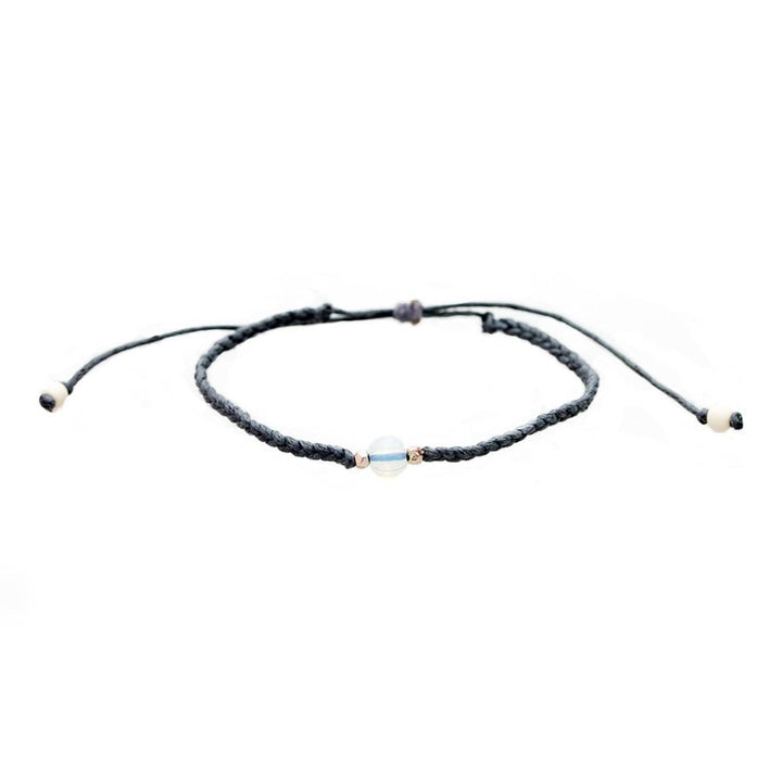 Close-up of a gray braided slip knot syle bracelet with a moonstone in the center and small gold accent beads on each side of the moonstone, displayed on a white background.