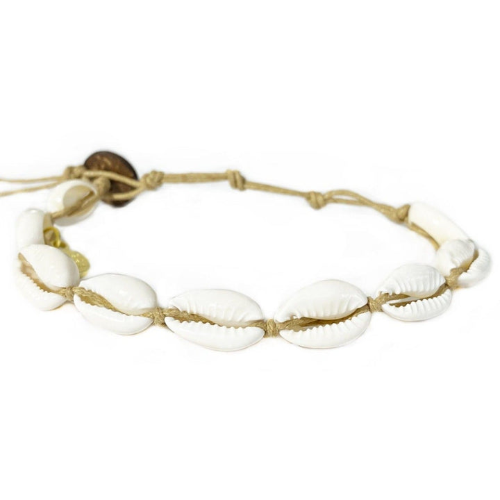 Close-up of a cowry shell bracelet made with nine white cowry sea shells strung on an adjustable natural tan color cord with a dark brown coconut shell button closure displayed on a white background.