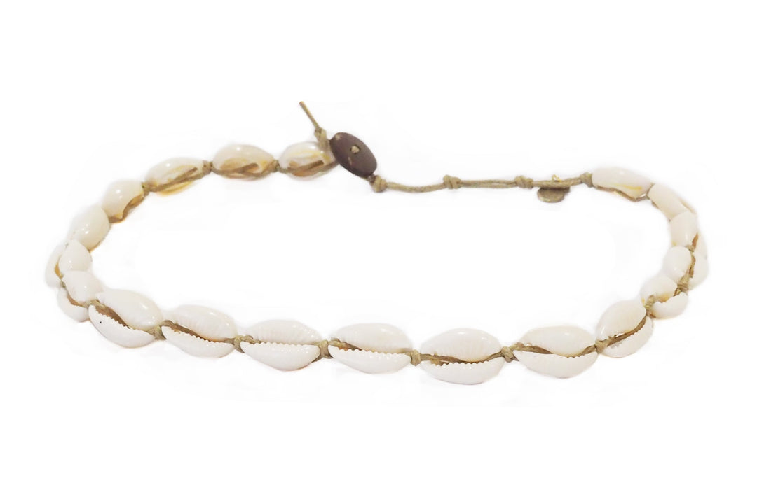 Close-up of a bracelet made with white cowry sea shells, strung on an adjustable tan cord with a coconut shell button closure, displayed on a white background.