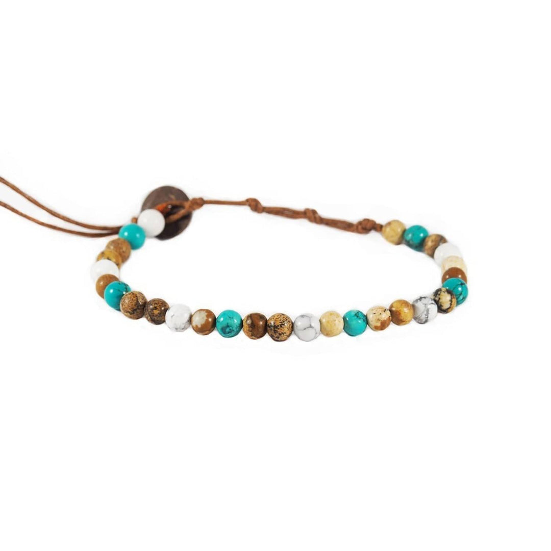 Close-up of a healing bead bracelet with round 6mm howlite and jasper beads in white, teal, and brown colors, with a adjustable brown cord and dark brown coconut shell button closure, displayed on a white background.