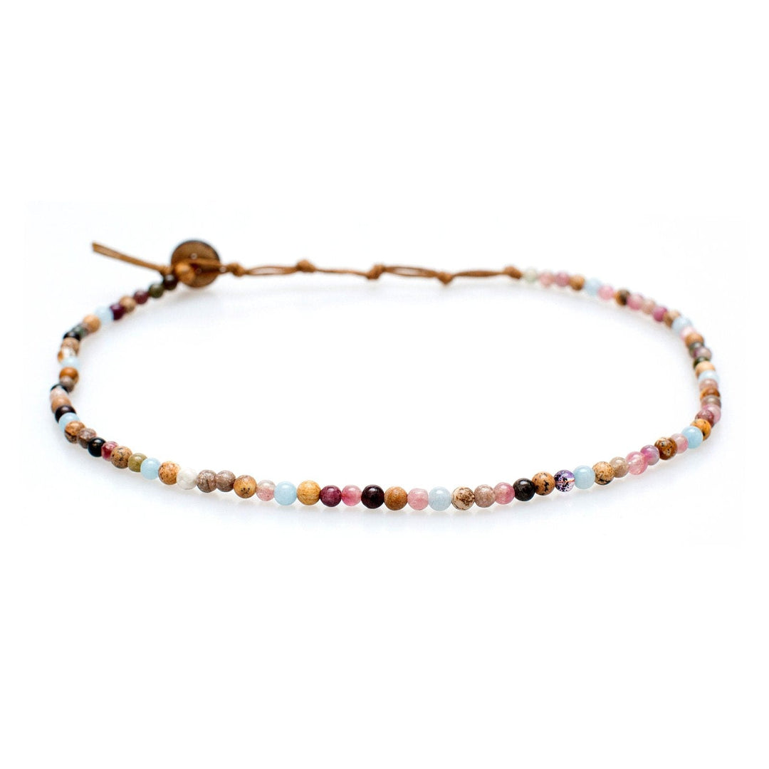 Close-up of a beaded necklace with 4mm Jasper and Tourmaline stone beads in shades of brown, pink, blue, deep purple, with tan cord and coconut button closure, displayed on a white background.