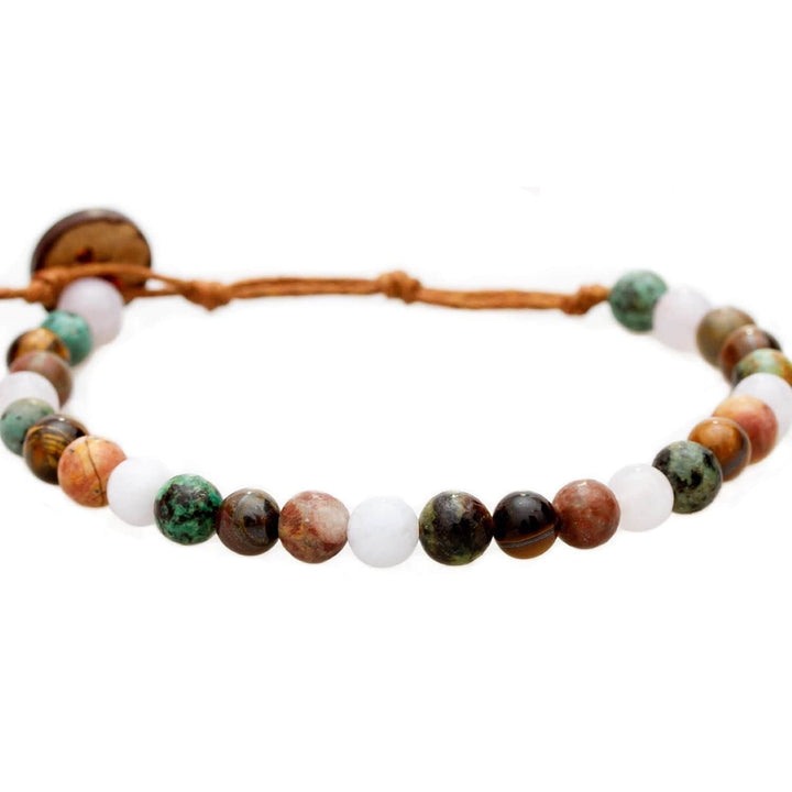 Close-up of a bead bracelet made with 6mm multicolor round jasper, and unakite, african turquoise beads, in shades of red, brown, and green colors, with a brown adjustable cord and a dark brown coconut shell button closure, displayed on a white background.