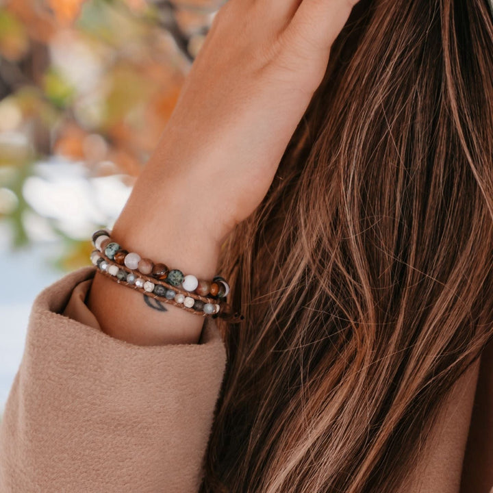 Close-up of a woman's wrist next to her long brown hair, wearing two bead bracelets in shades of brow, green, tan, and white.