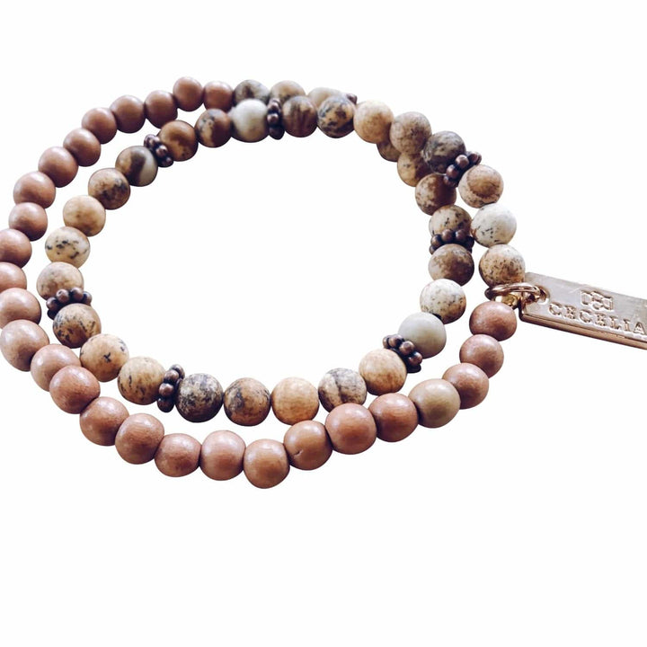 A stretch syle double-wrap bracelet made with picture jasper beads with shades of brown, and brown wood, beads with copper accent beads, and a gold-tone logo tag, displayed on a white background.