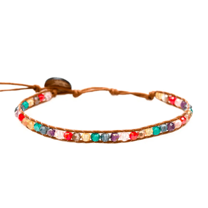 Close-up of a beaded wrap bracelet with bright colored crystals in blush pink, red, yellow, green, blue, and purple, with an adjustable brown cord and coconut button closure, displayed on a white bakground.
