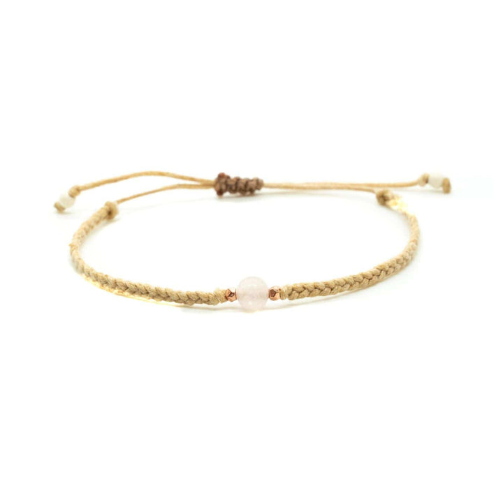 Close-up of a braided slip knot syle bracelet with a rose quartz bead in the center and two accent beads on each side, displayed on a white background.