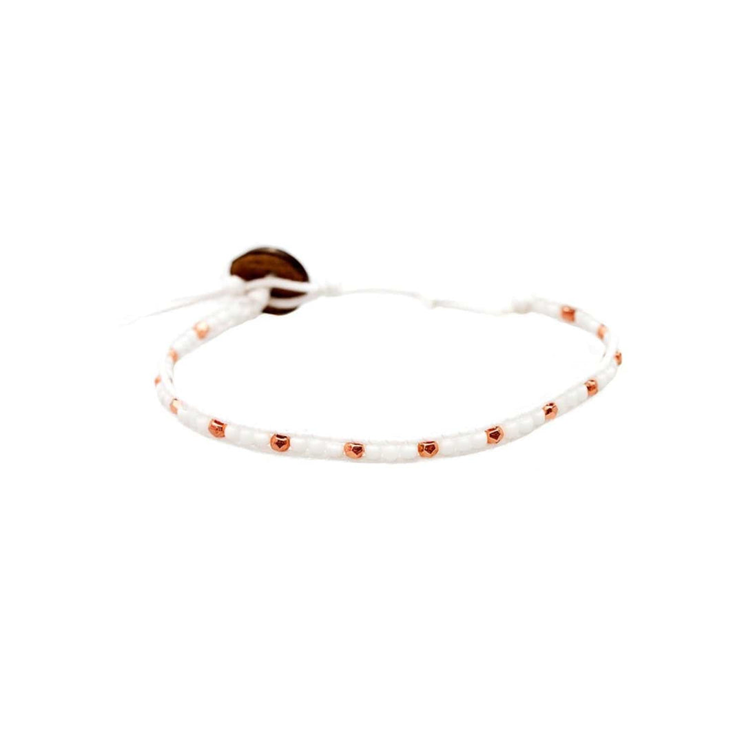 Close-up of a wrap style bead bracelet made with white and rose gold seed beads, an adjustable white cord with a coconut shell button closure, displayed on a white background.