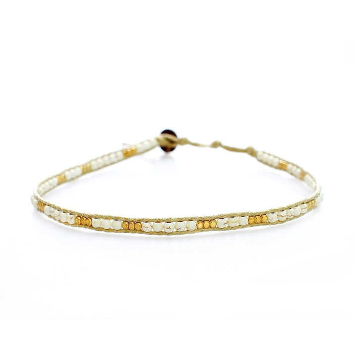 Close-up of a choker style necklace made with white and tan imitation howlite beads, and gold tone beads, strung on an adjustable cream white cord with a coconut shell button closure, displayed on a white background.