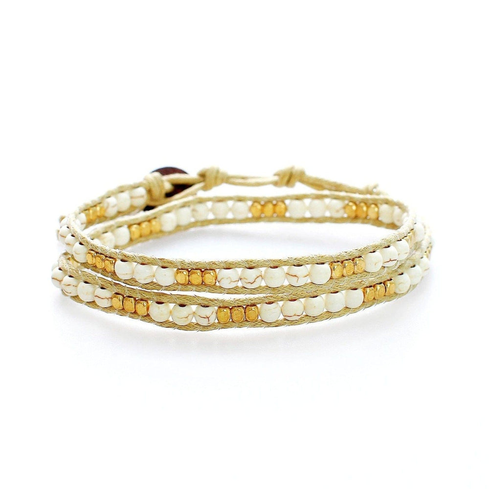 Close-up of a double wrap bracelet, that can be worn as a choker, made with white and tan imitation howlite beads, and gold tone beads, strung on an adjustable cream white cord with a coconut shell button closure, displayed on a white background.