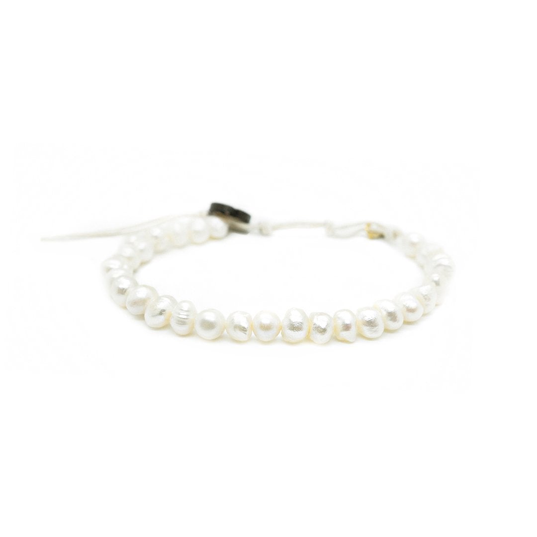 Close-up of a bead bracelet made with white fresh water pearls, and white adjustable cord, with a dark brown coconut shell button closure, displayed on a white background.