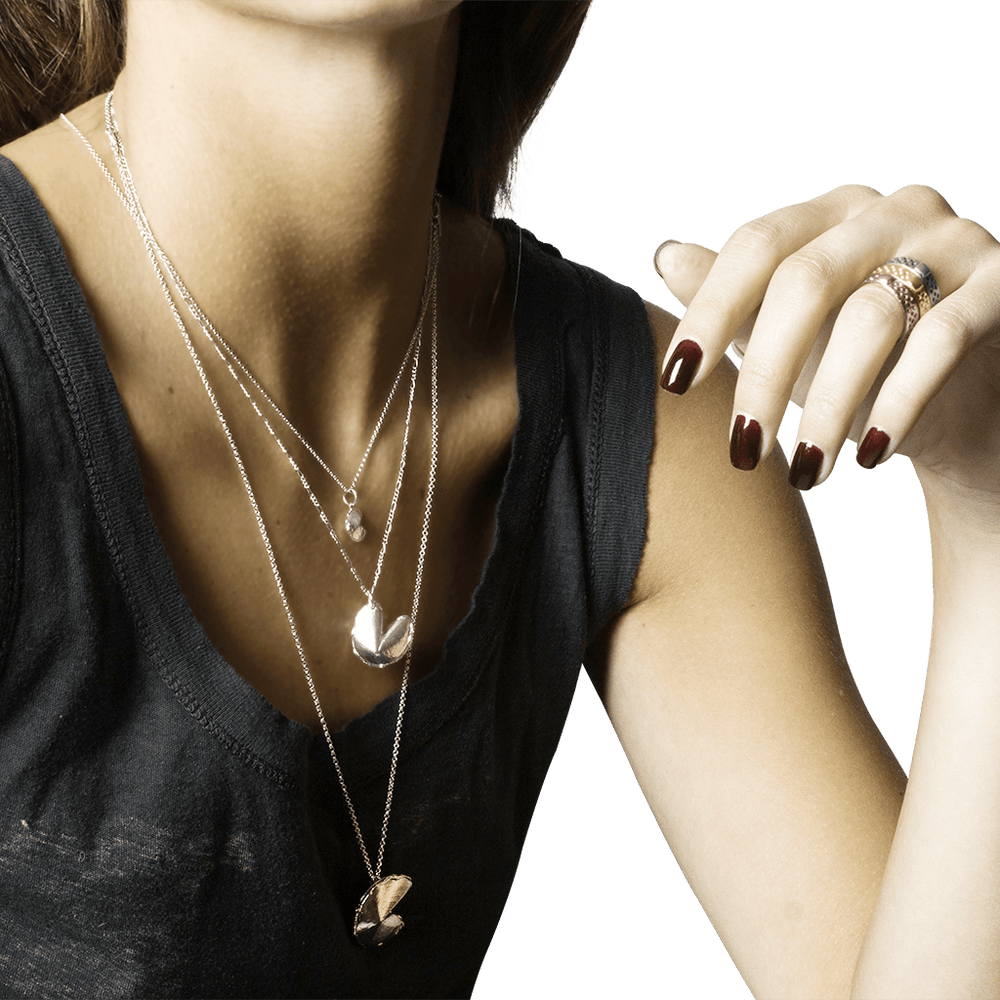 Close-up of a woman's neck, chest, and arm; wearing a gray shirt and three silver necklaces in different lengths, each with a different size fortune cookie charm.