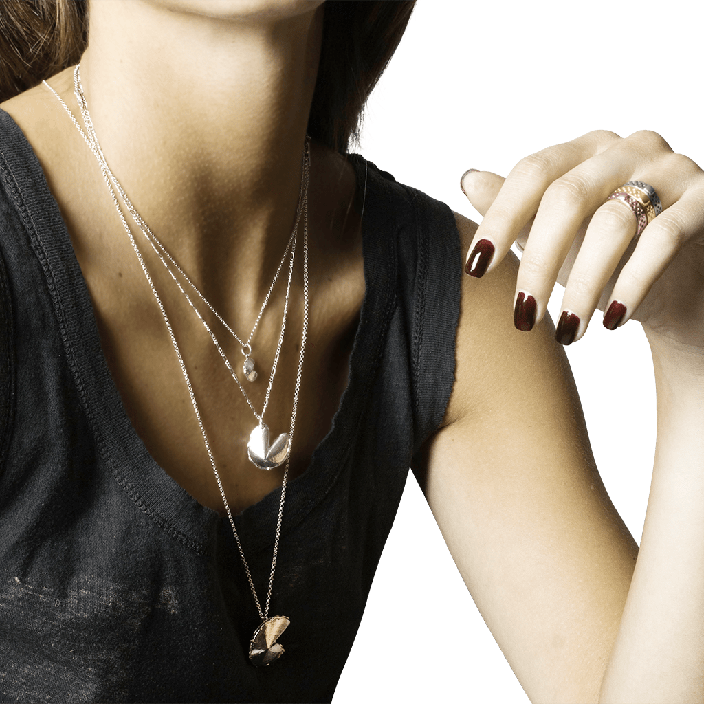 Close-up of a woman's neck, chest, and arm; wearing a gray shirt and three silver necklaces in different lengths, each with a different size fortune cookie charm.