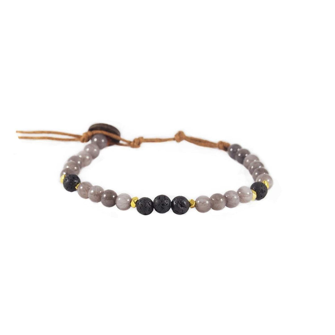 Close-up of a healing bead bracelet with round 6mm lava stone and quartz beads in purplish gray and black colors, and gold accent beads, with a adjustable brown cord and dark brown coconut shell button closure, displayed on a white background. 