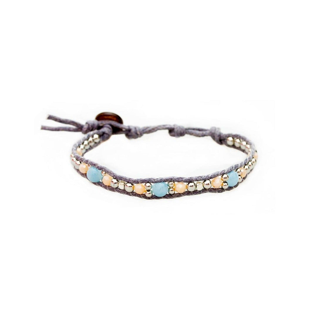 Close-up of a wrap style bead bracelet made with light blue amazonite beads, pale orange crystal beads, and shiny silver metal beads, strung on an adjustable gray cord with a brown coconut shell button closure.