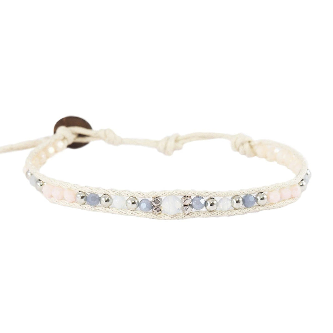 Close-up of a wrap bracelet with a center moonstone, smaller moonstones, creamy white and gray crystals, silver accent beads, a white adjustable cord with coconut button, displayed on a white background.