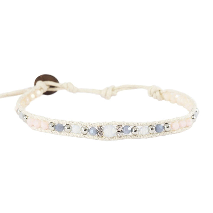 Close-up of a wrap bracelet with a center moonstone, smaller moonstones, creamy white and gray crystals, silver accent beads, a white adjustable cord with coconut button, displayed on a white background.