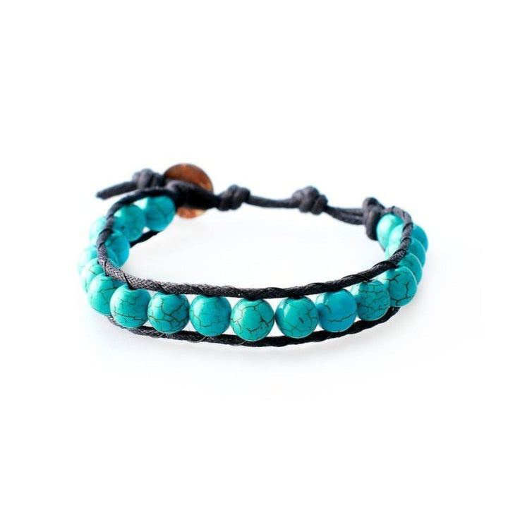 Close-up of a men's wrap bracelet with round 6mm imatation cracked turquoise beads in black and turquoise blue colors, with a adjustable black cord and dark brown coconut shell button closure, displayed on a white background.
