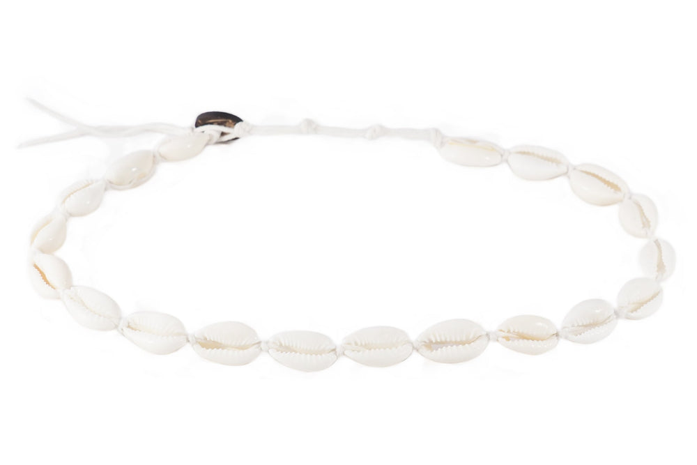 Close-up of a bracelet made with white cowry sea shells, strung on an adjustable white cord with a coconut shell button closure, displayed on a white background.