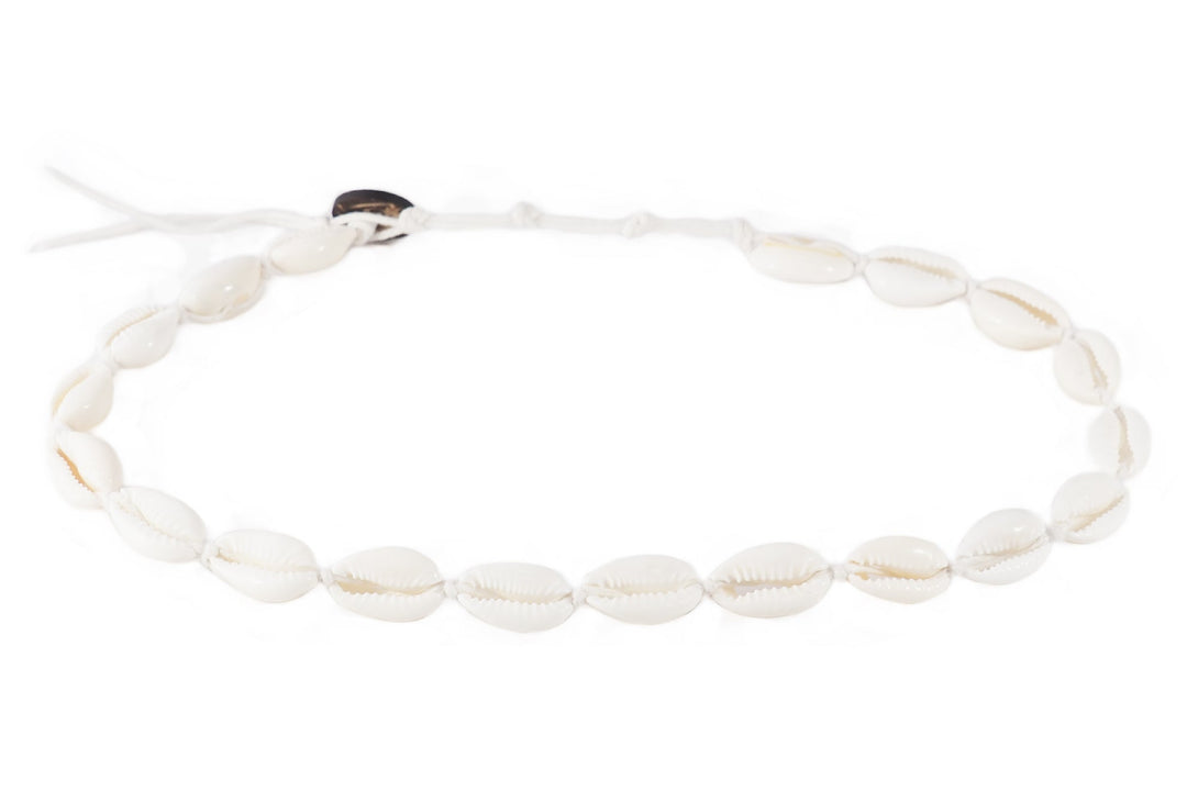 Close-up of a bracelet made with white cowry sea shells, strung on an adjustable white cord with a coconut shell button closure, displayed on a white background.