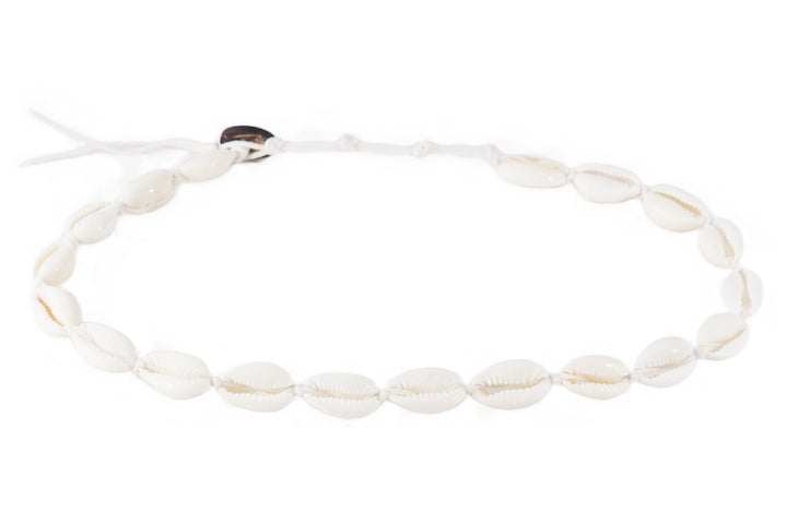 Close-up of a bracelet made with white cowry sea shells, strung on an adjustable white cord with a coconut shell button closure, displayed on a white background.