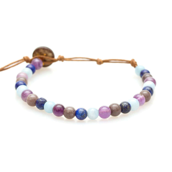 Close-up of a healing bead bracelet made with 6mm multicolor round lapis lazuli and amethyst beads, in shades of blue, purple, and tan colors, and an adjustable brown cord with a dark brown coconut shell button closure, displayed on a white background.