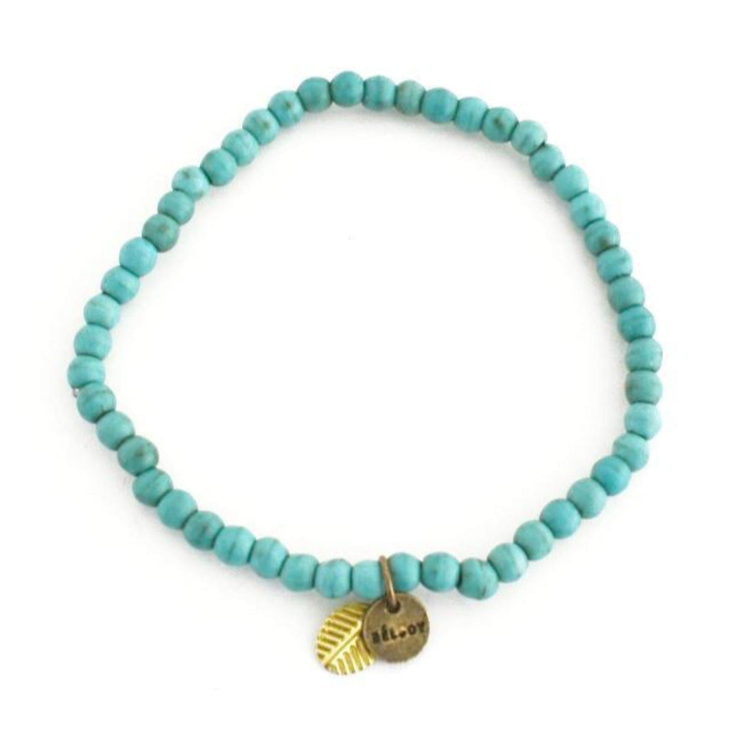 A turquoise lava stone bead bracelet with 4mm round beads, a gold brass leaf bead accent, and a gold brass beljoy logo charm, displayed on a white background.